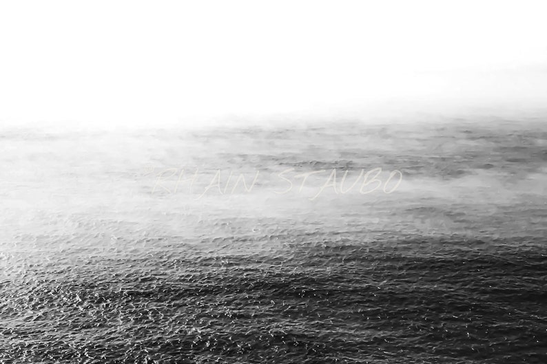 May include: A black and white photograph of a foggy ocean. The water is choppy and the fog is thick, creating a sense of mystery and depth.