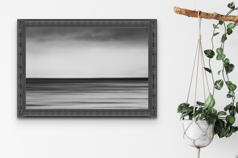 May include: A black and white photograph of a calm ocean with a cloudy sky. The photo is framed in a black ornate frame.