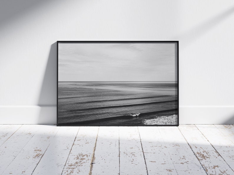 May include: Black and white photograph of ocean waves crashing on the shore. The photo is framed in a black frame.