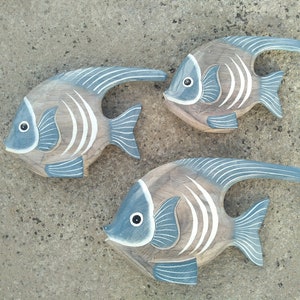 May include: Three wooden fish wall decor in shades of brown and blue with white accents. The fish are carved with details and have a distressed finish.