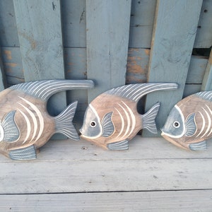May include: Three wooden fish wall decor in shades of brown and blue with white stripes. The fish are arranged in a row, with the largest fish on the left and the smallest fish on the right.