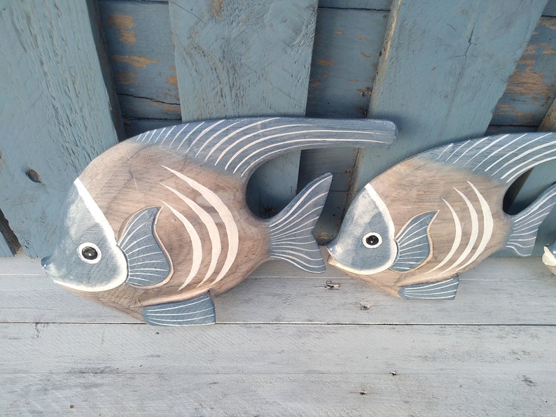 May include: Two wooden fish wall decor with a blue and white painted design. The fish are carved in a realistic style and have a 3D effect.