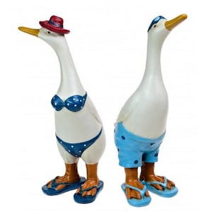 May include: Two white duck figurines wearing blue and white swimwear and flip-flops. The female duck is wearing a red hat and a blue and white polka dot bikini. The male duck is wearing blue and white polka dot swim trunks.