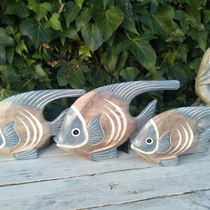 May include: Three wooden fish sculptures in shades of brown and blue, with white stripes. The fish are arranged in a row, with the largest fish in the back and the smallest fish in the front.