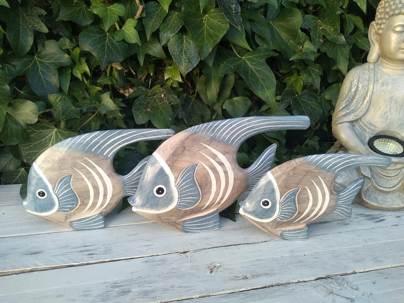 May include: Three wooden fish sculptures in shades of brown and blue, with white stripes. The fish are arranged in a row, with the largest fish in the back and the smallest fish in the front.