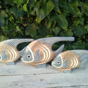 May include: Three wooden fish sculptures in shades of brown and blue, with white stripes. The fish are arranged in a row, with the largest fish in the back and the smallest fish in the front.