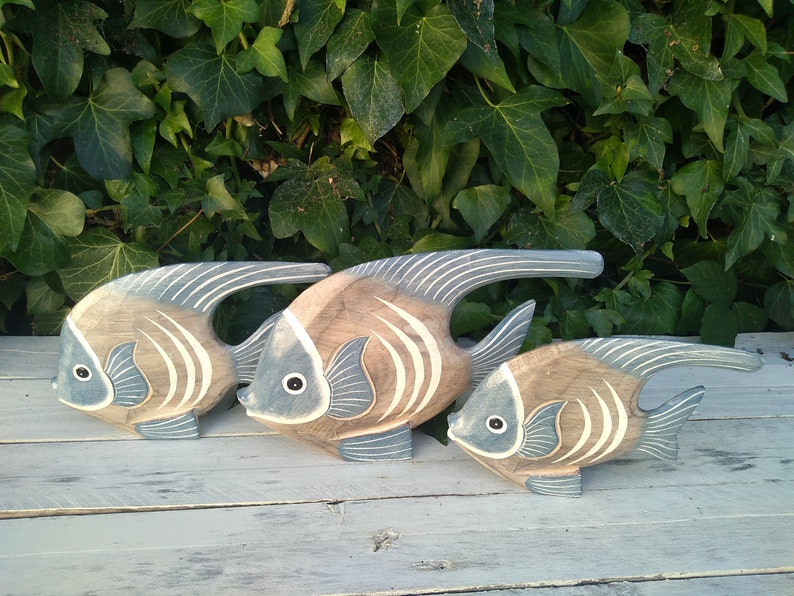 May include: Three wooden fish sculptures in shades of brown and blue, with white stripes. The fish are arranged in a row, with the largest fish in the back and the smallest fish in the front.