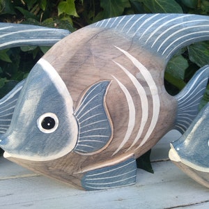 May include: Three wooden fish sculptures painted in shades of blue and brown. The fish have white stripes and black eyes.