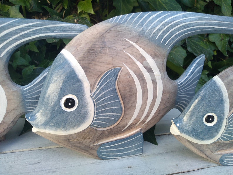 May include: Three wooden fish sculptures painted in shades of blue and brown. The fish have white stripes and black eyes.