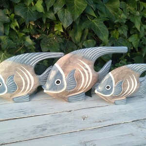 May include: Three wooden fish sculptures in shades of brown and blue, arranged in a row from largest to smallest. The fish have a stylized design with white stripes and are painted with a distressed finish.