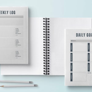 May include: Two spiral bound notebooks with gray covers. The left notebook has the text "WEEKLY LOG" and is divided into sections for each day of the week. The right notebook has the text "DAILY GOALS" and is divided into sections for each day of the week.