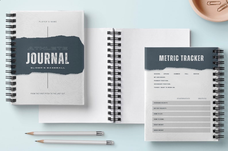 May include: A white and gray spiral bound journal with a gray torn paper overlay. The text on the cover reads "Athlete Journal" and "Slider's Baseball". The journal has a section for "Metric Tracker" with columns for "Spring", "Summer", "Fall", and "Winter".