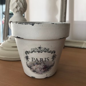 May include: White ceramic flower pot with a distressed finish. The pot has a floral design and the word "PARIS" printed on it.