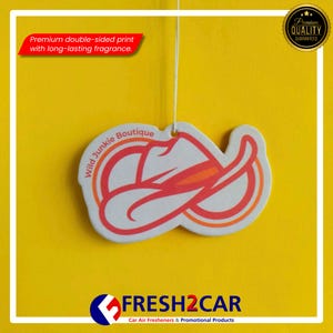 May include: A white car air freshener shaped like a cowboy hat with red and orange accents, hanging against a yellow background. The text "Wild Junkie Boutique" is visible on the freshener. The image also includes the text "Premium double-sided print with long-lasting fragrance."