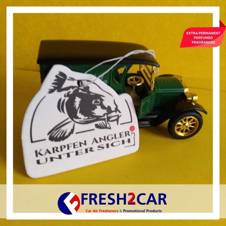 May include: A car air freshener with the text "KARPFEN ANGLER UNTER SICH" and a carp illustration, hanging in front of a green and black vintage car model. The freshener is white with black text and a black illustration. The car model has gold wheels.