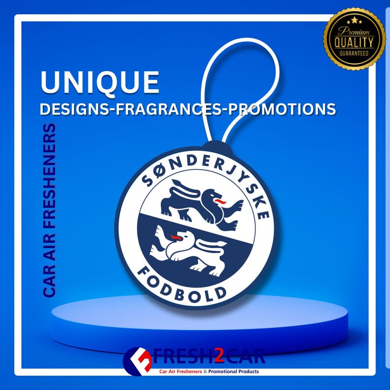 May include: A round car air freshener with a white string, featuring a blue and white logo with text. The logo includes the words "S&Oslash;NDERJYSKE FODBOLD" and two stylized lion-like creatures. The background is blue with the words "UNIQUE DESIGNS-FRAGRANCES-PROMOTIONS".