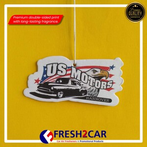 May include: A car air freshener with a classic car design, the text "US MOTORS" and an eagle graphic. The freshener has a double-sided print and long-lasting fragrance. The background is yellow.
