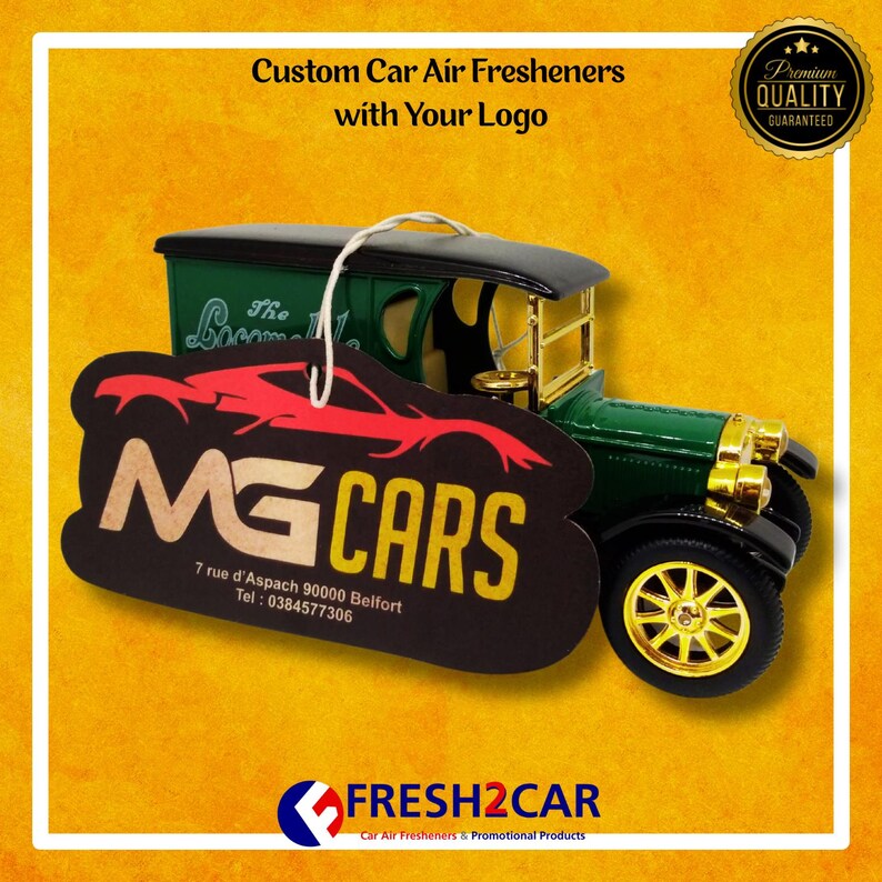 Pu&ograve; includere: Un modello di auto d'epoca verde e oro con un profumatore per auto personalizzato con la scritta "MG CARS" e l'indirizzo. Il profumatore per auto &egrave; nero con una grafica di auto rossa. L'immagine include anche il testo "Custom Car Air Fresheners with Your Logo."