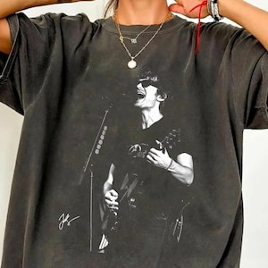 以下が含まれることがあります： 黒い持ち手と「But First, Coffee」の文字が黒い手書き風フォントで書かれた白いセラミックマグ。マグカップは白い表面に置かれています。