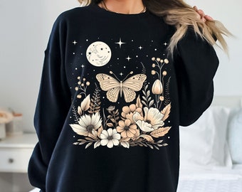 May include: Black sweatshirt with a floral and butterfly design. The design features a moon, stars, and flowers in shades of beige and brown.