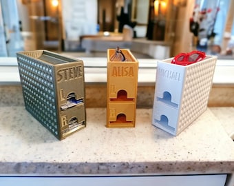 Könnte beinhalten: Drei 3D-gedruckte Aufbewahrungsboxen für Brillen, jede mit einem anderen Namen auf der Vorderseite: Steve, Alisa und Michael. Die Boxen sind in verschiedenen Farben: grün, orange und weiß.