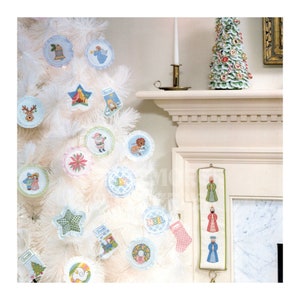 May include: A white artificial Christmas tree decorated with handmade felt ornaments. The ornaments feature various Christmas themes, including a star, a reindeer, a bell, and a dove. The tree is decorated with a variety of colors, including red, blue, green, and pink. There is a small felt stocking hanging on the tree. The tree is standing on a white surface. There is a small felt Christmas tree on the mantle above the fireplace.