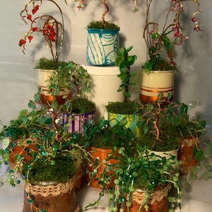 May include: A selection of handmade wire and bead sculptures, crafted to resemble miniature trees. These are planted in small, decorated tin cans, some with twine detailing. The beads are in various colours, including green, red, and pink.