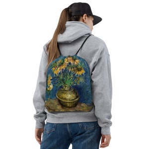 May include: A drawstring backpack with a print of a painting of a vase of yellow flowers on a blue background.
