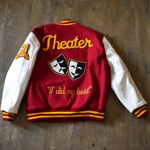 May include: Red and white varsity jacket with "Theater" embroidered in yellow script. Features white sleeves, yellow and red striped cuffs, and the phrase "I did my best". Includes a patch with the number "31".