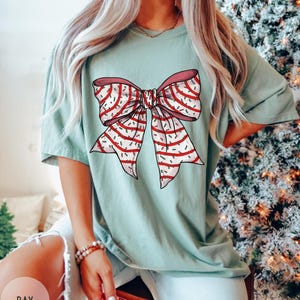 May include: A light blue t-shirt with a red and white striped bow with green and white sprinkles on it.