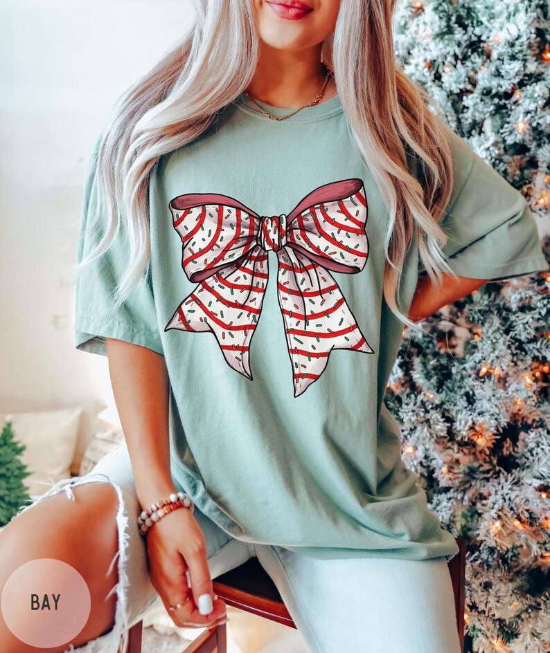 May include: A light blue t-shirt with a red and white striped bow with green and white sprinkles on it.