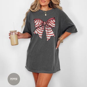 May include: A gray oversized t-shirt with a red and white striped bow graphic. The bow has a pink center.
