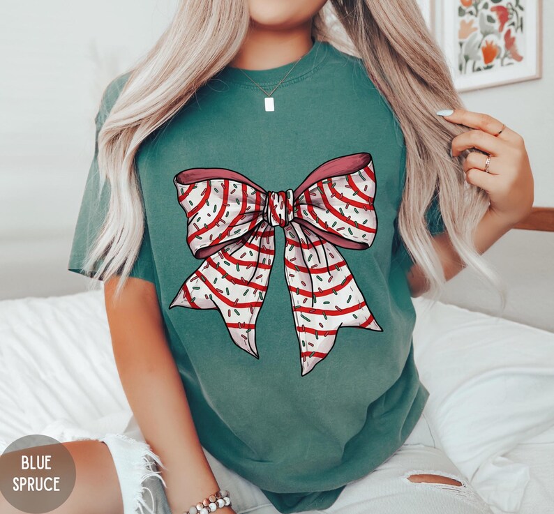 May include: A teal green t-shirt with a white and red bow with sprinkles on it.