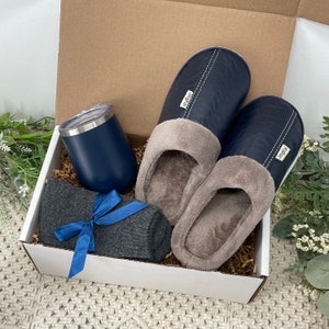 May include: A gift box filled with a pair of blue slippers, a gray pair of socks, and a blue tumbler. The box is lined with brown paper.