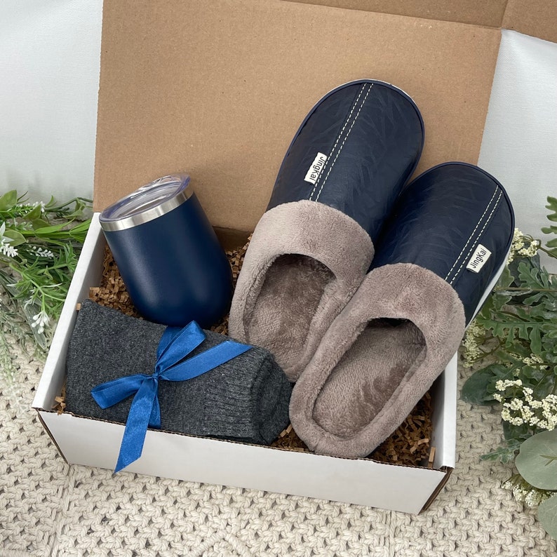 May include: A gift box filled with a pair of blue slippers, a gray pair of socks, and a blue tumbler. The box is lined with brown paper.