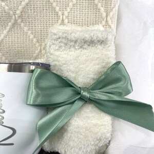 May include: A gift basket with a white fuzzy blanket, a white mug with a black design, and a green satin ribbon.