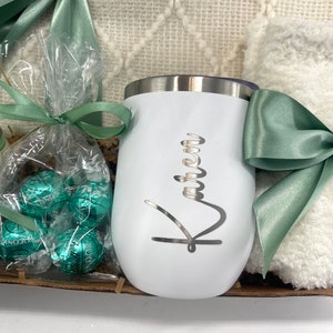 May include: A white insulated tumbler with the name "Karen" engraved on it. The tumbler is part of a gift basket that includes a blanket, chocolates, and a green ribbon.