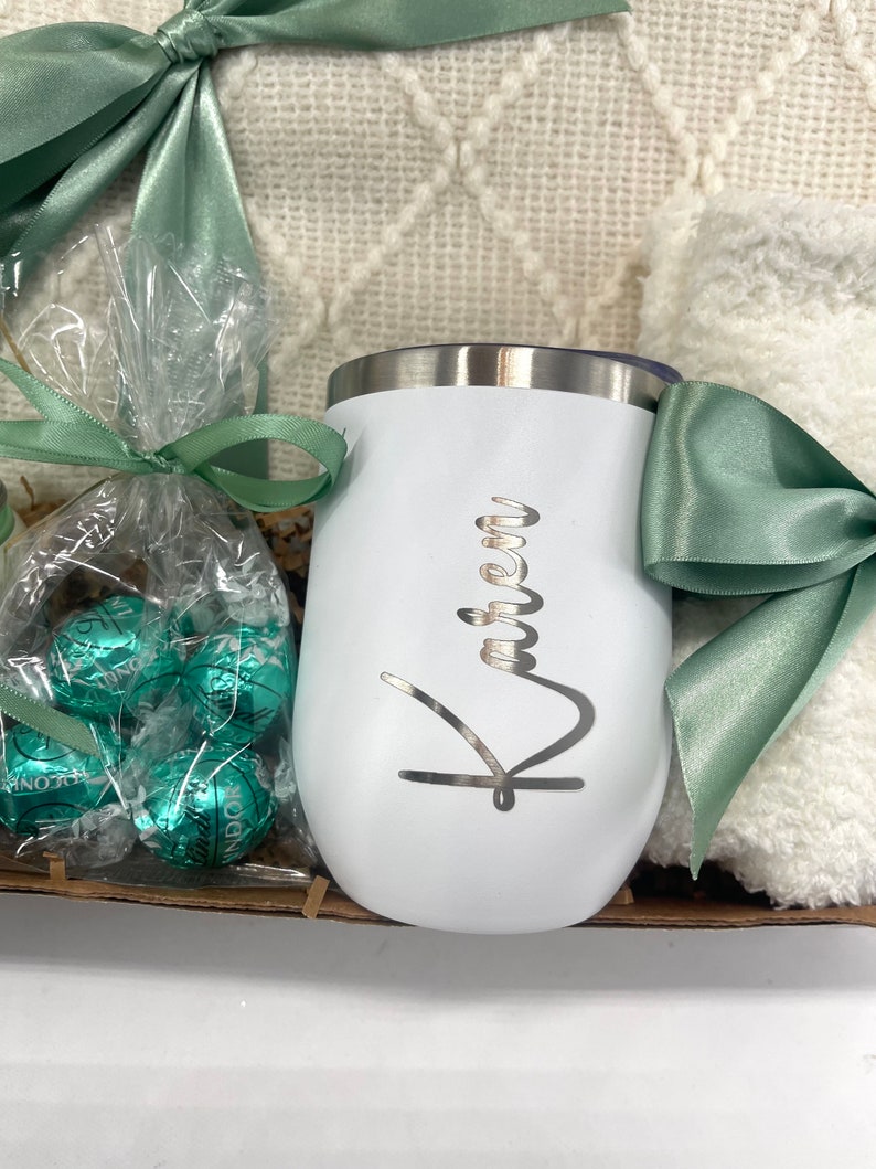 May include: A white insulated tumbler with the name "Karen" engraved on it. The tumbler is part of a gift basket that includes a blanket, chocolates, and a green ribbon.