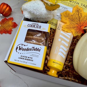 May include: A gift box with fall-themed items. It includes a box of lemon cookies, a tube of hand cream, a pumpkin-shaped container, and decorative fall leaves. The cookies are glazed with lemon meringue and weigh 3 oz (85 g).