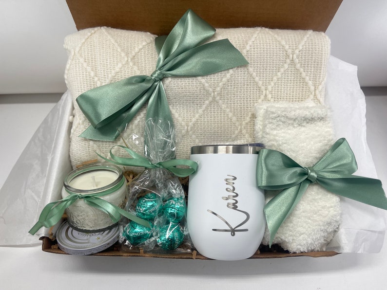 May include: A gift basket filled with a white blanket, a white mug with the name "Karen" on it, a white candle, a bag of green chocolate candies, and a pair of white fuzzy socks.