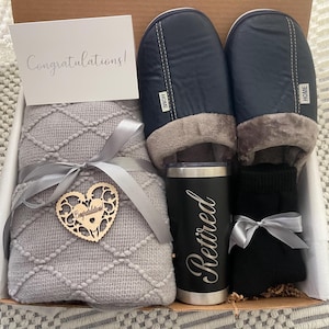 Peut inclure: Un panier-cadeau contenant une couverture en tricot gris, une paire de pantoufles noires, une tasse de voyage noire avec le mot "Retrait&eacute;" grav&eacute; dessus et une paire de chaussettes noires. Le panier comprend &eacute;galement un c&oelig;ur en bois avec le mot "F&eacute;licitations !" dessus.
