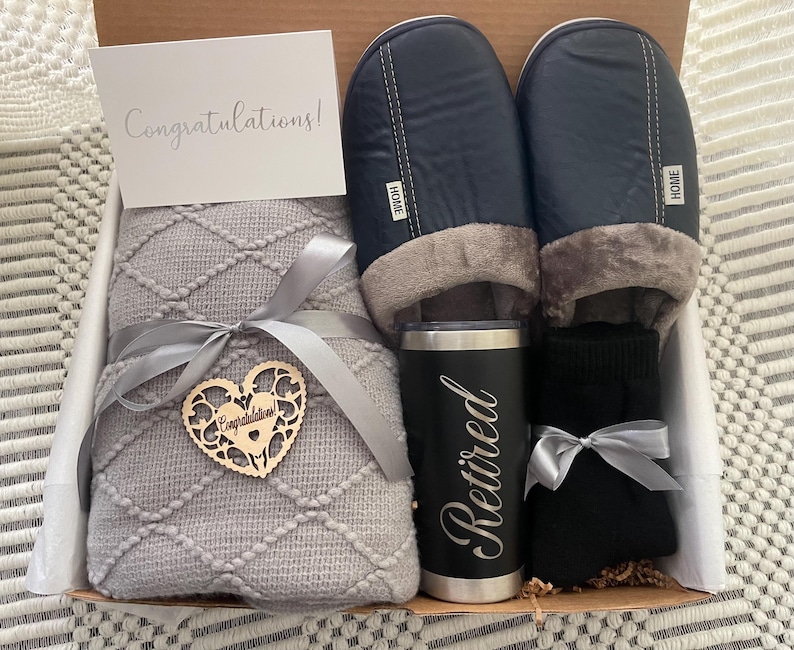 Peut inclure: Un panier-cadeau contenant une couverture en tricot gris, une paire de pantoufles noires, une tasse de voyage noire avec le mot "Retrait&eacute;" grav&eacute; dessus et une paire de chaussettes noires. Le panier comprend &eacute;galement un c&oelig;ur en bois avec le mot "F&eacute;licitations !" dessus.