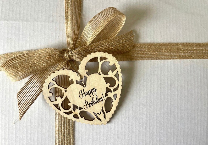 May include: A brown gift box with a brown burlap ribbon and bow. A wooden heart-shaped tag with the text "Happy Birthday!" is attached to the ribbon.