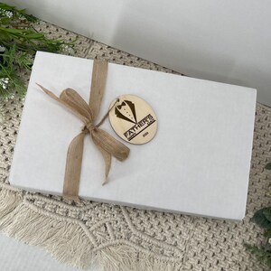 May include: A white gift box with a brown ribbon and a wooden tag that says "Happy Father's Day 2023".