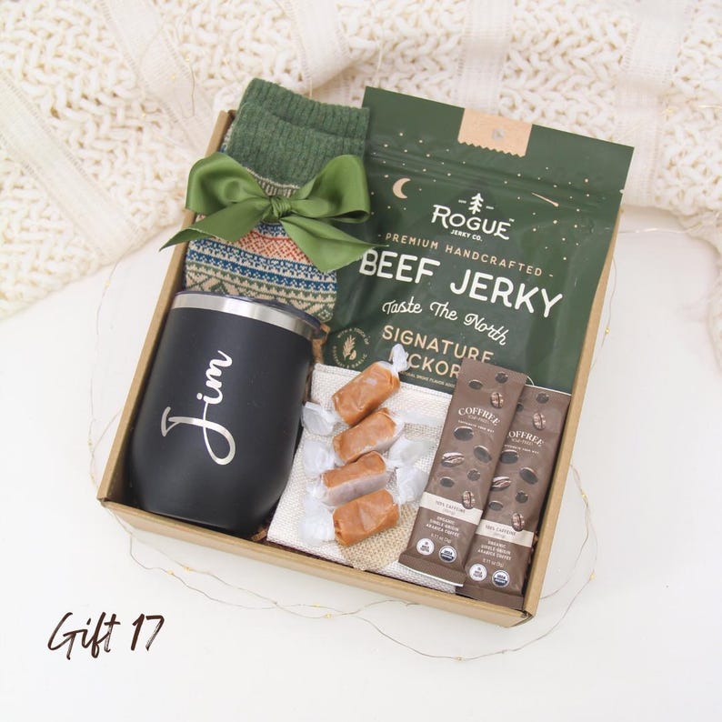Puede incluir: Una caja de regalo que contiene un vaso negro con "Jim" en escritura cursiva, calcetines verdes, un lazo verde, carne seca, barras de caf&eacute; y caramelos envueltos. La caja es marr&oacute;n.