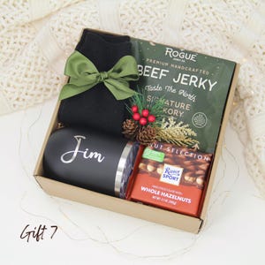 Puede incluir: Una caja de regalo con un vaso negro con "Jim" en plata, carne seca, una tableta de chocolate y calcetines negros atados con un lazo verde. La caja est&aacute; decorada con pi&ntilde;as y bayas. La tableta de chocolate pesa 100g.