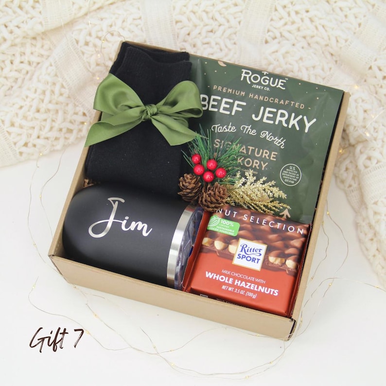 Puede incluir: Una caja de regalo con un vaso negro con "Jim" en plata, carne seca, una tableta de chocolate y calcetines negros atados con un lazo verde. La caja est&aacute; decorada con pi&ntilde;as y bayas. La tableta de chocolate pesa 100g.