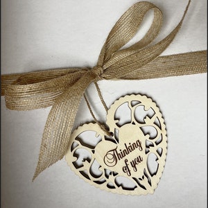 May include: A wooden heart-shaped tag with a cutout design and the text "Thinking of you" in a cursive font. The tag is tied to a brown burlap ribbon.