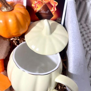 May include: A fall-themed gift basket with a pumpkin-shaped mug, a pumpkin spice chai tea packet, a chocolate bar, and a small pumpkin.