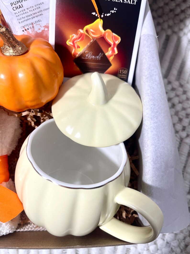 May include: A fall-themed gift basket with a pumpkin-shaped mug, a pumpkin spice chai tea packet, a chocolate bar, and a small pumpkin.